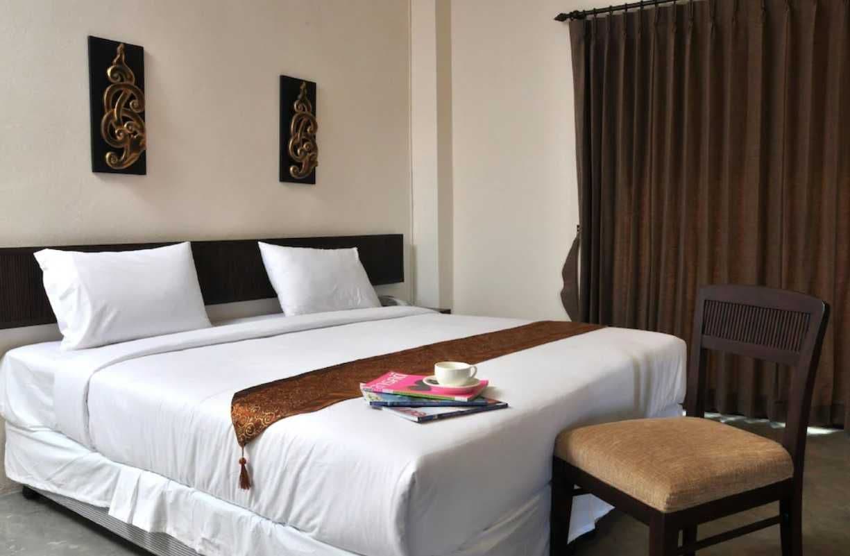 A hotel room with a large bed, a bedside table with a cup and books, and a chair.