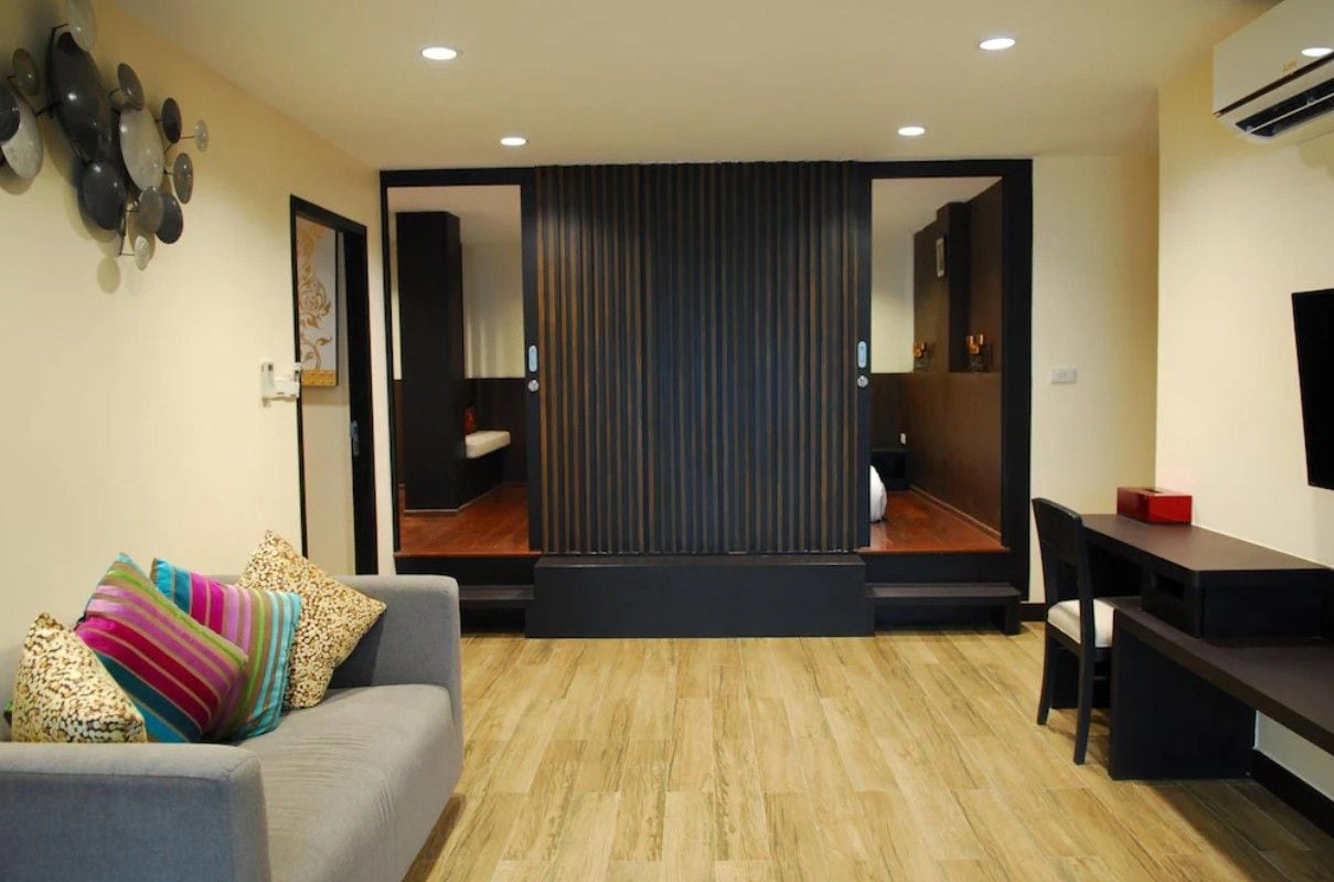 A modern living room with a sofa, a dining table, and a kitchen area visible through a sliding door.