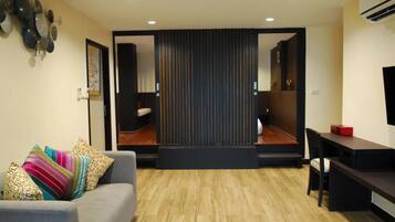 A modern living room with a sofa, a dining table, and a kitchen area visible through a sliding door.