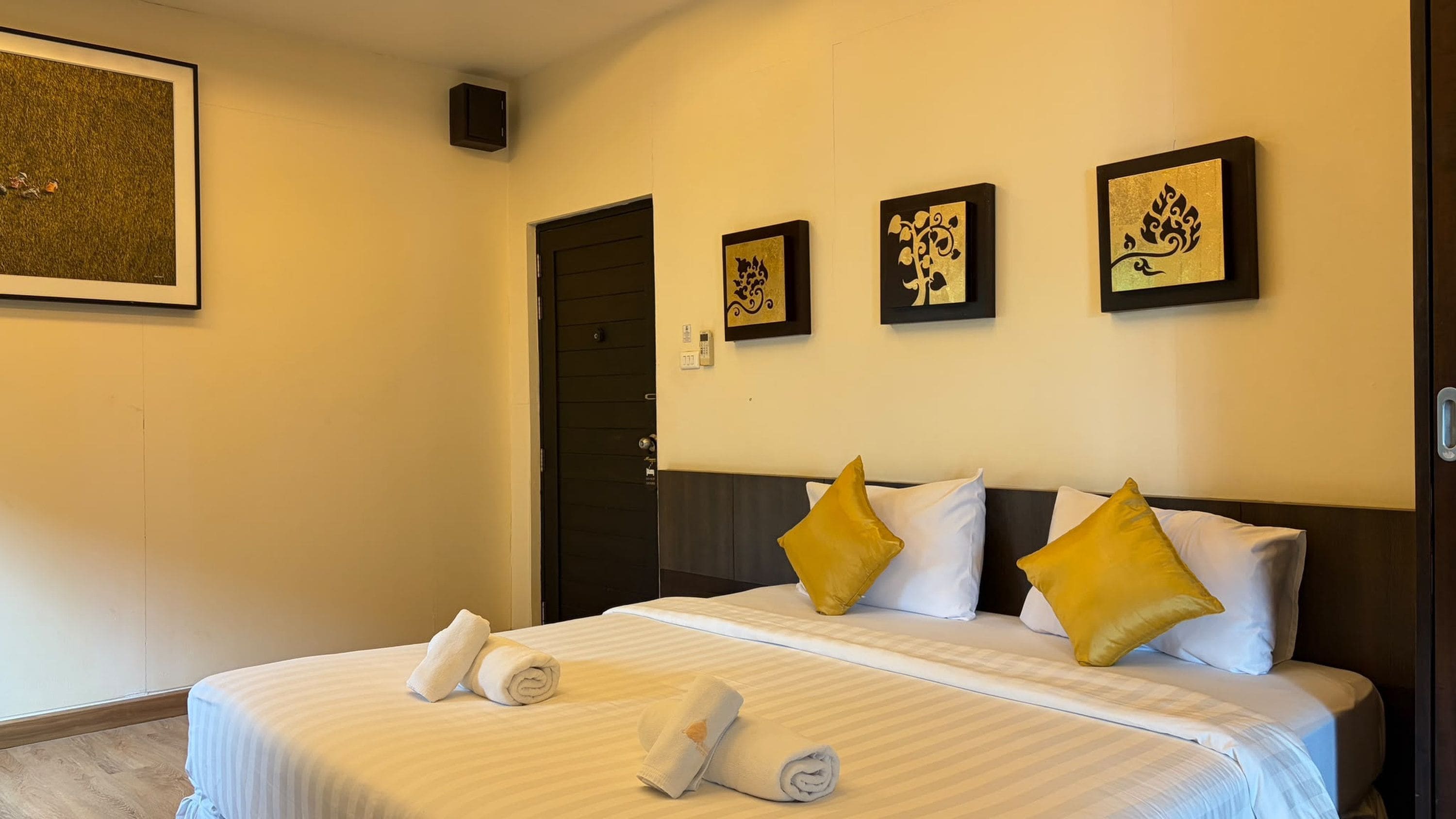 A hotel room with a bed, pillows, a wall-mounted artwork, and a door.