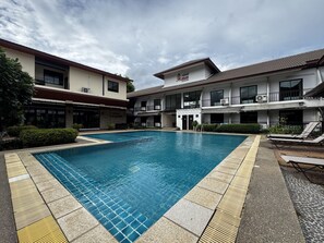 Una piscina con borde de azulejos, rodeada por un edificio con varios balcones y unidades de aire acondicionado.