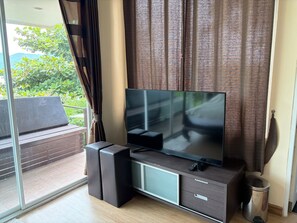 A modern living room with a flat-screen TV on a wooden cabinet, a sliding glass door leading to an outdoor area, and a metal trash can.