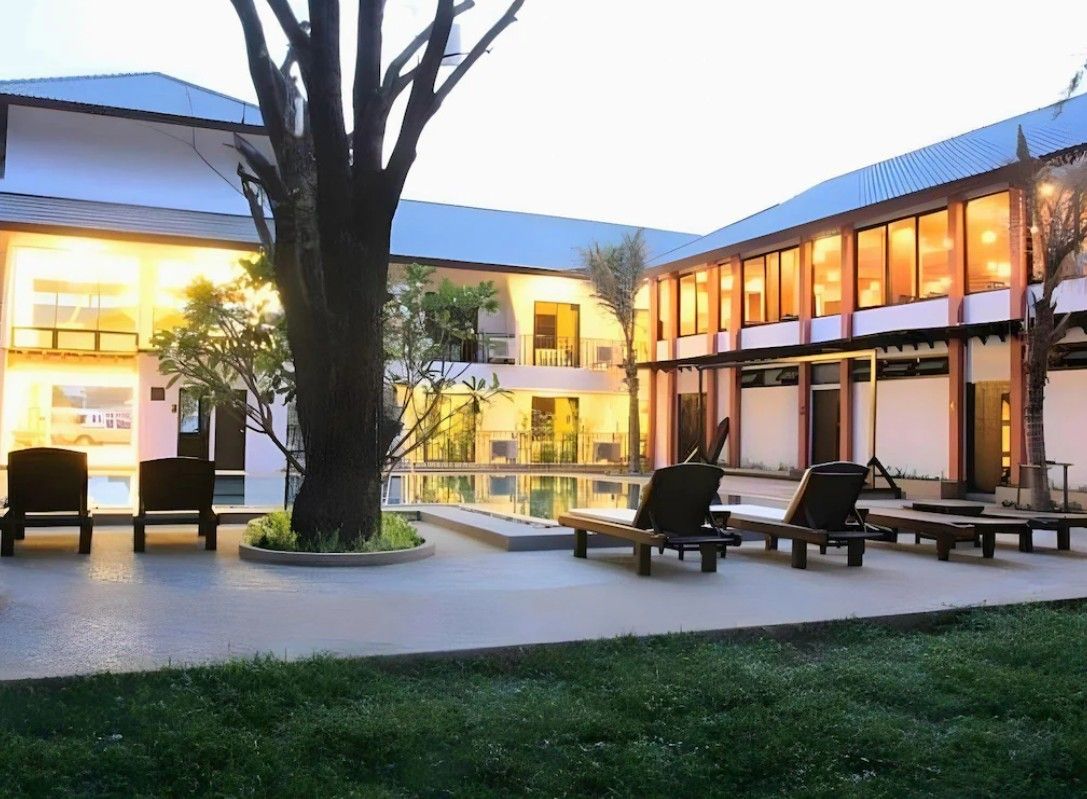 A hotel courtyard with lounge chairs, a large tree, and a building with multiple windows.