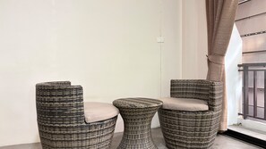 A corner with two wicker chairs and a small round table, a white wall, and a window with curtains.
