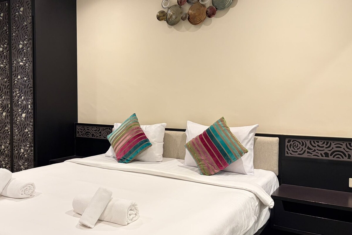 Un lit bien fait, avec du linge de lit blanc et deux coussins décoratifs, une tête de lit noire et un élément décoratif fixé au mur au-dessus du lit.