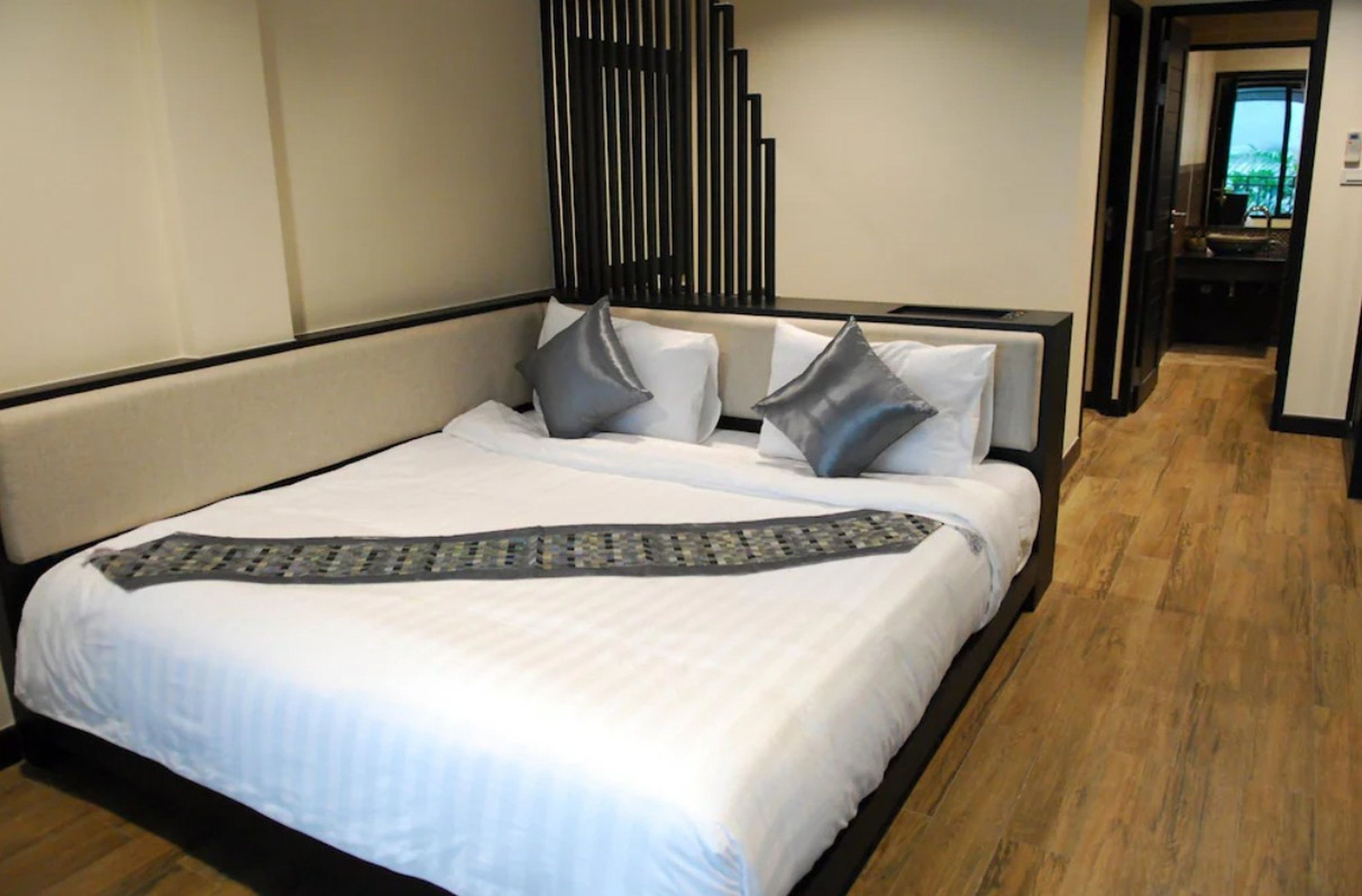 A hotel room with a large bed, a headboard, and a wooden floor.