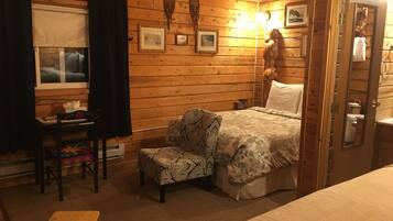 A cozy room with a bed, a chair, a desk, and a window with curtains.