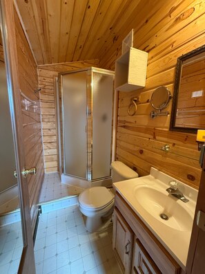 A wooden-paneled bathroom with a toilet, sink, and shower. - Earthsong Lodge (Healy)