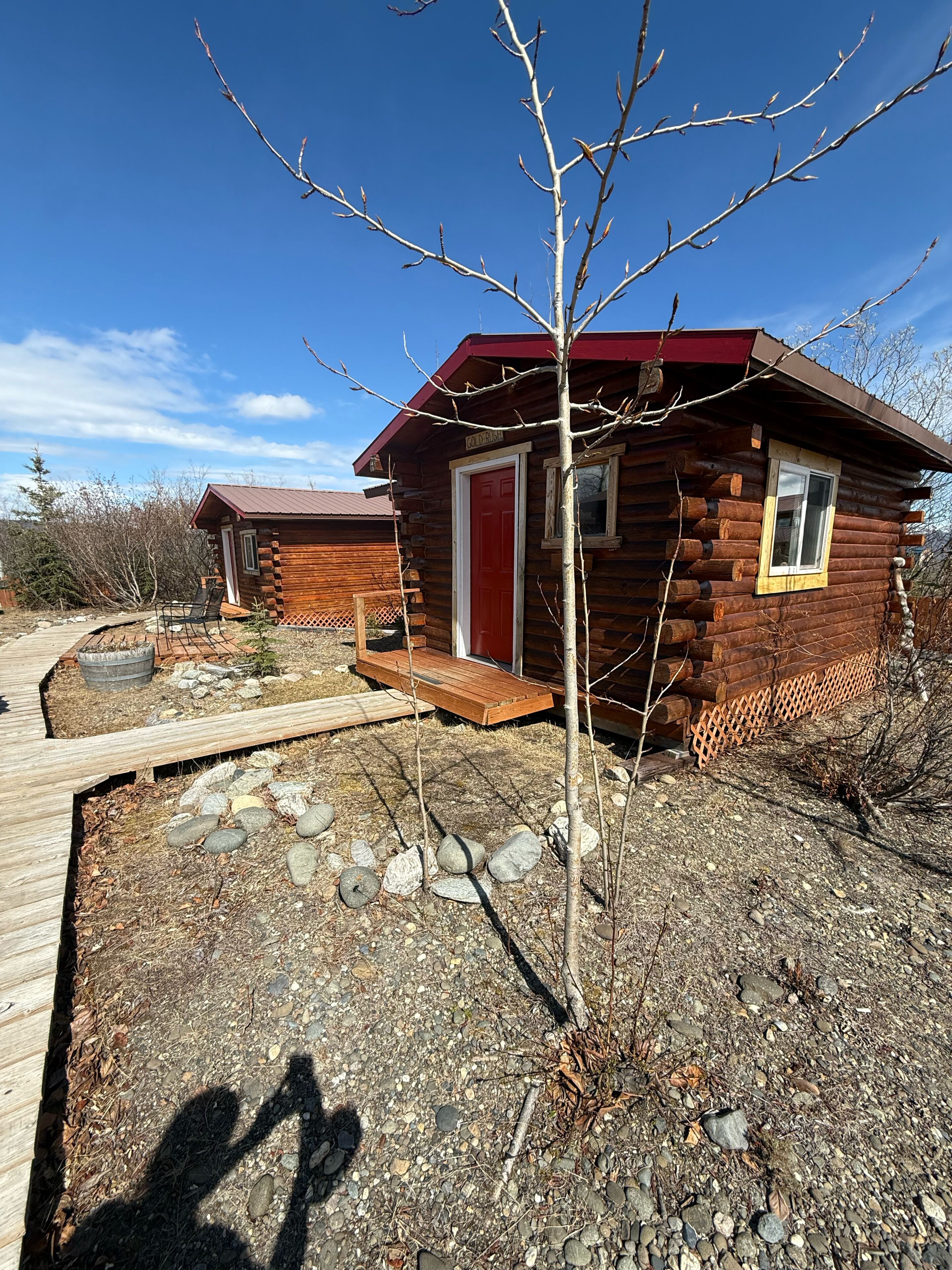 Eine Blockhütte mit roter Tür, einer Holzterrasse und blauem Himmel.