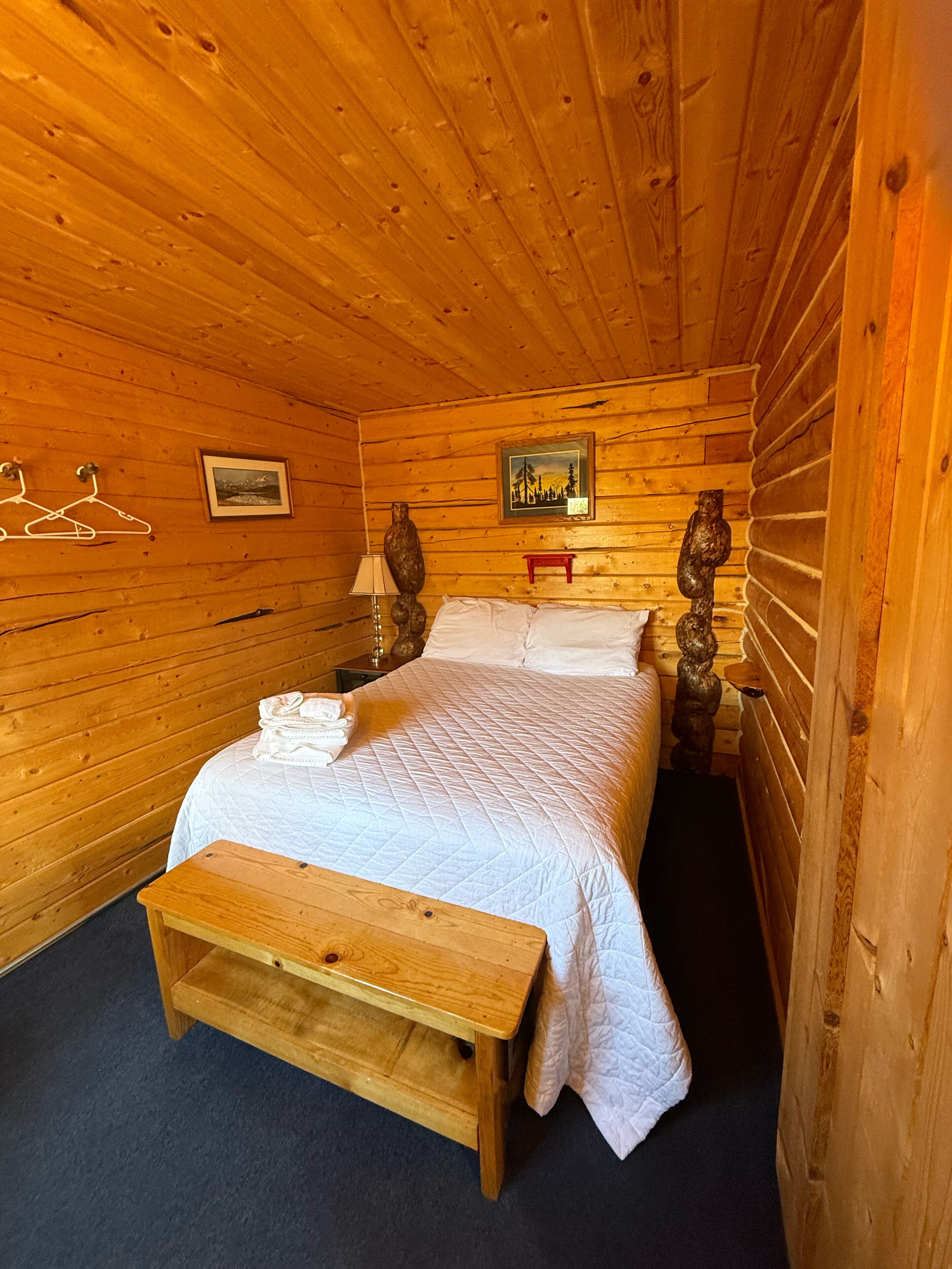 Une chambre à coucher dans un chalet en bois, avec un lit, des tables de chevet, un luminaire suspendu et un tableau encadré au mur.