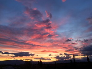 A sunset over a mountainous landscape with silhouettes of trees and a road leading towards the horizon. - Earthsong Lodge (Healy)