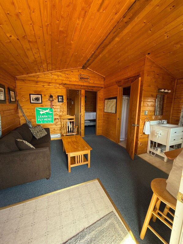 A cozy cabin interior with a wooden ceiling, a sofa, a small table, a desk, and a bed. - Earthsong Lodge (Healy)