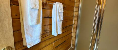 A wooden interior with a shower, a toilet, and towels hanging on the wall.