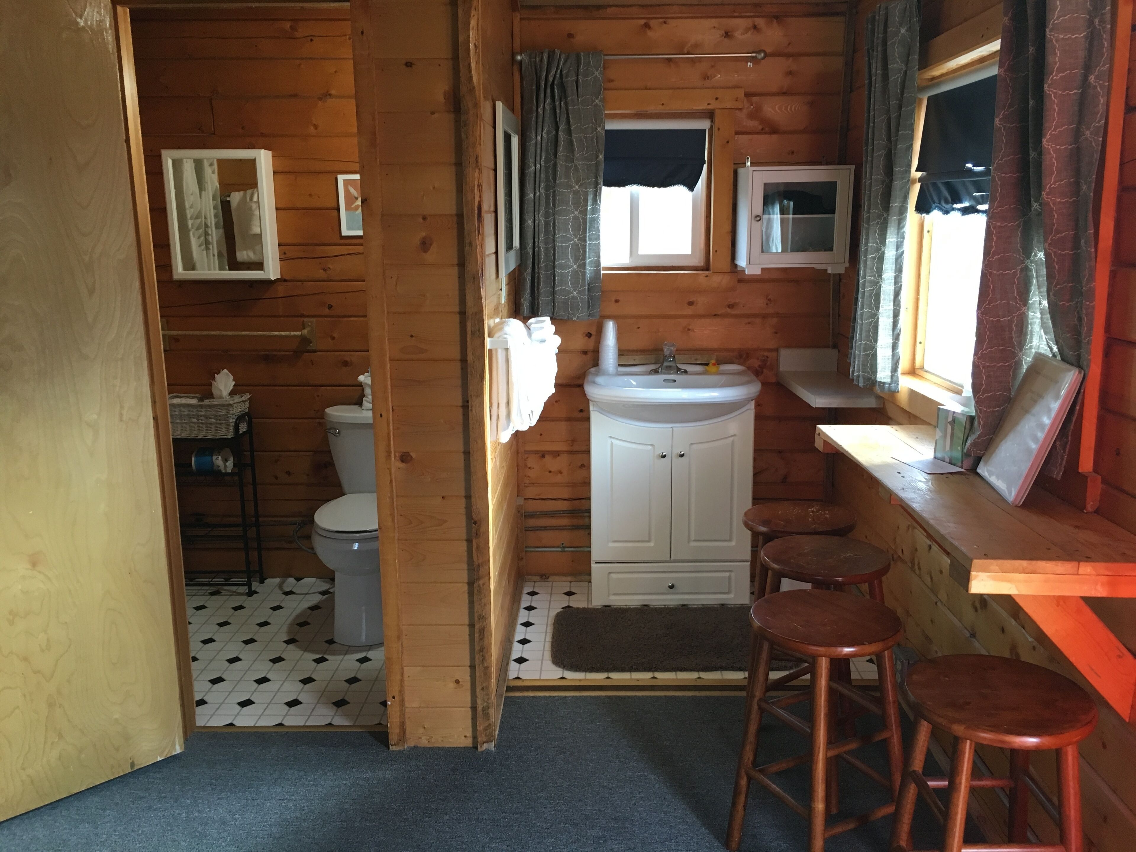 A compact wooden cabin bathroom with a toilet, sink, and two stools.