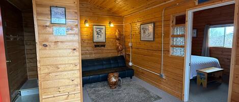Interior d'una cabana de fusta amb una banca de fusta, un cartell de benvinguda, imatges emmarcades i una taula petita.