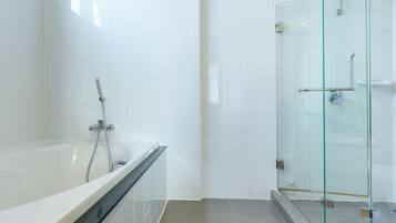A modern bathroom with a glass-enclosed shower, a bathtub with a black edge, and white tiled walls.