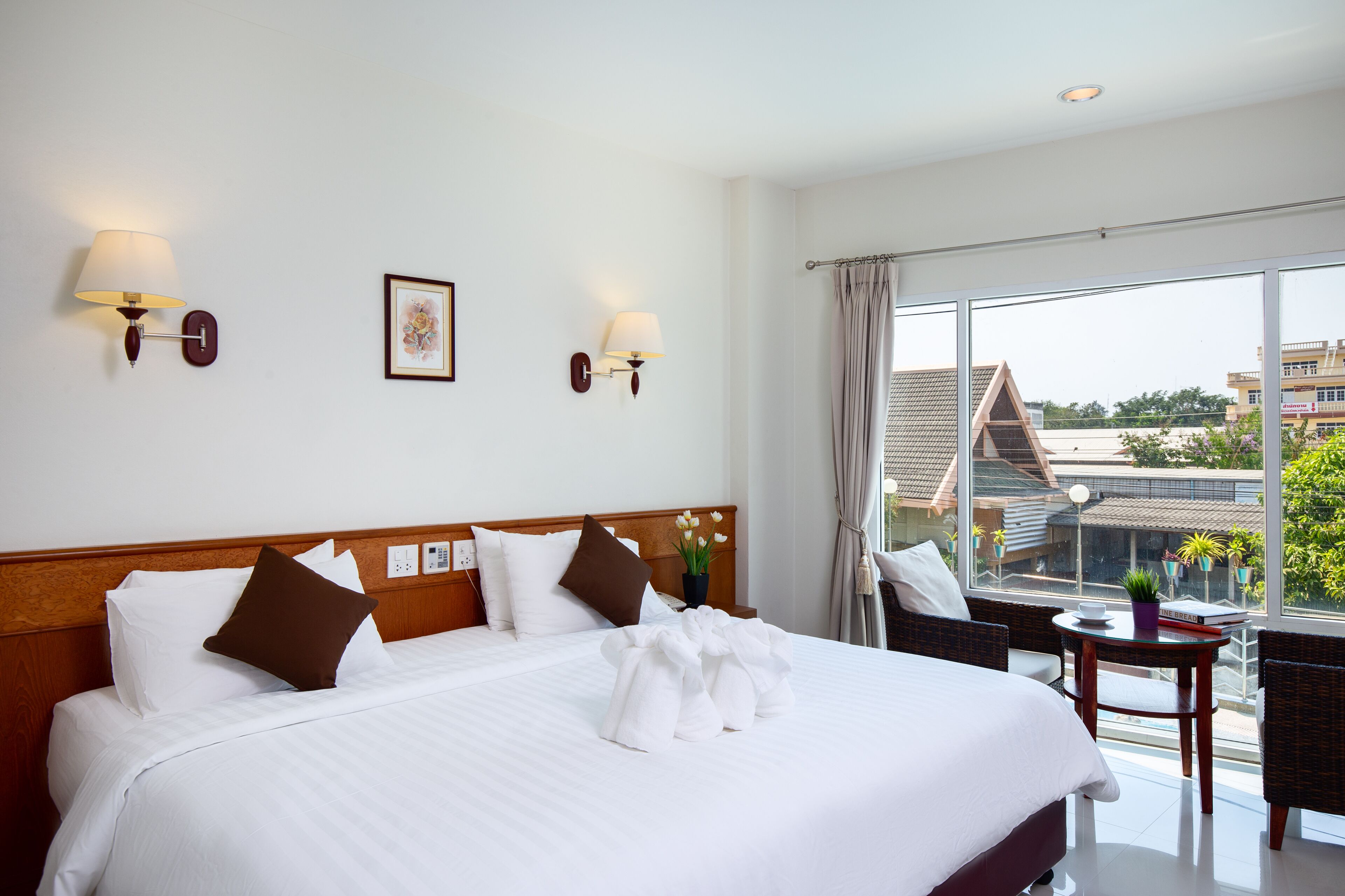 Ein Hotelzimmer mit einem großen Bett, zwei Wandlampen, einem Fenster mit Blick auf Gebäude und einem kleinen Tisch mit einer Pflanze.