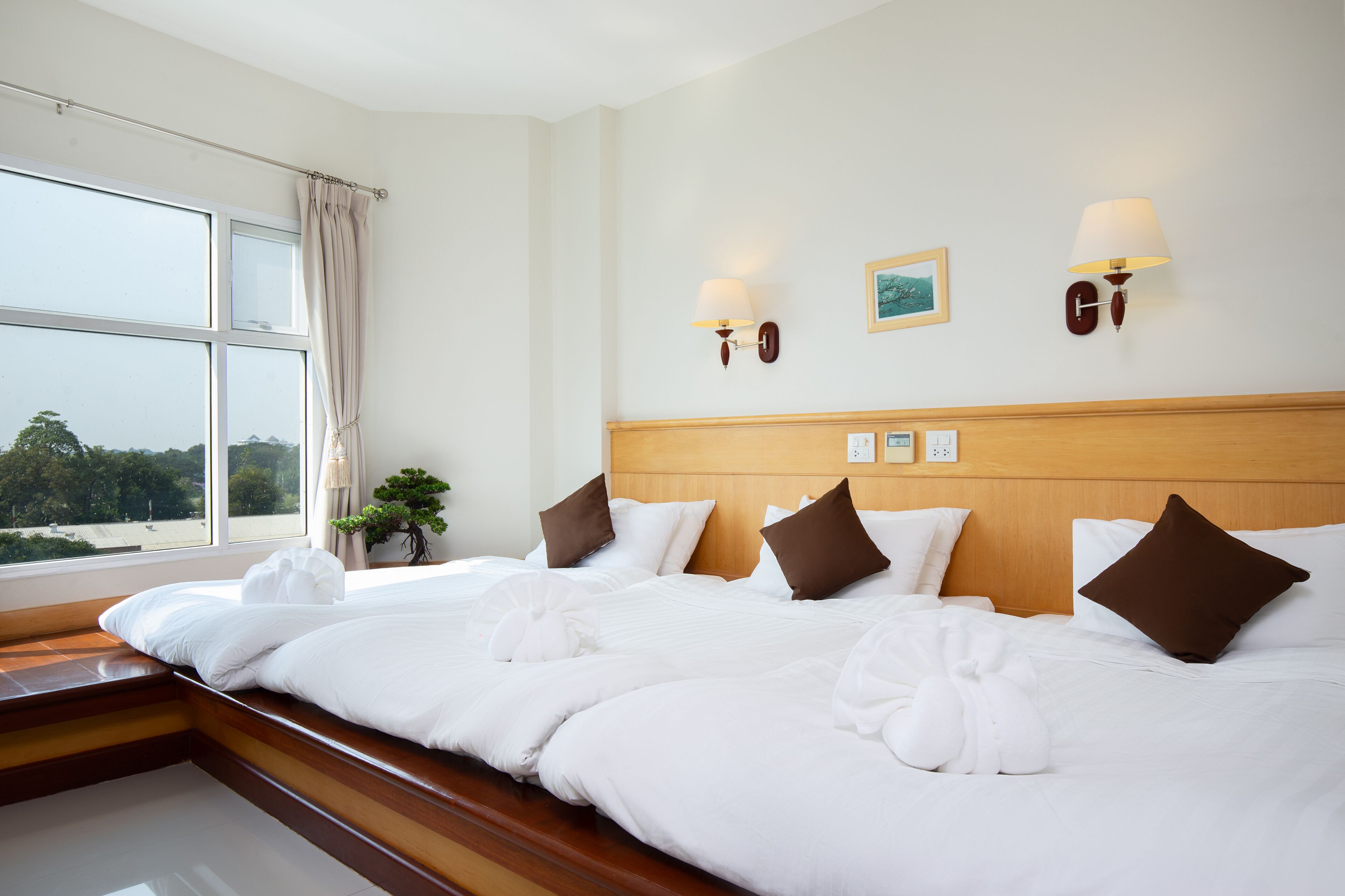 A hotel room with a large bed, wooden headboard, two wall-mounted lamps, and a window with curtains.