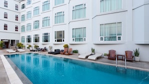 A swimming pool with lounge chairs and potted plants, surrounded by a white building with multiple windows. - Kanchanaburi City Hotel (Kanchanaburi)