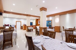 Uma ampla sala de jantar com várias mesas e cadeiras, uma mesa de recepção e uma parede com um pôster.