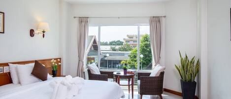 A hotel room with a large bed, two armchairs, a small table, and a potted plant.