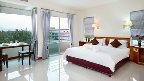 A hotel room with a bed, a desk with chairs, a view of the city, and a balcony. - Kanchanaburi City Hotel (Kanchanaburi)