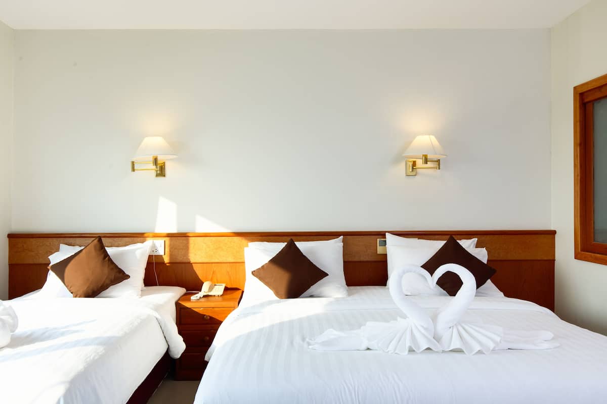 A hotel room with two beds, each with white linens and brown pillows. There are wall-mounted lamps on either side of the beds.