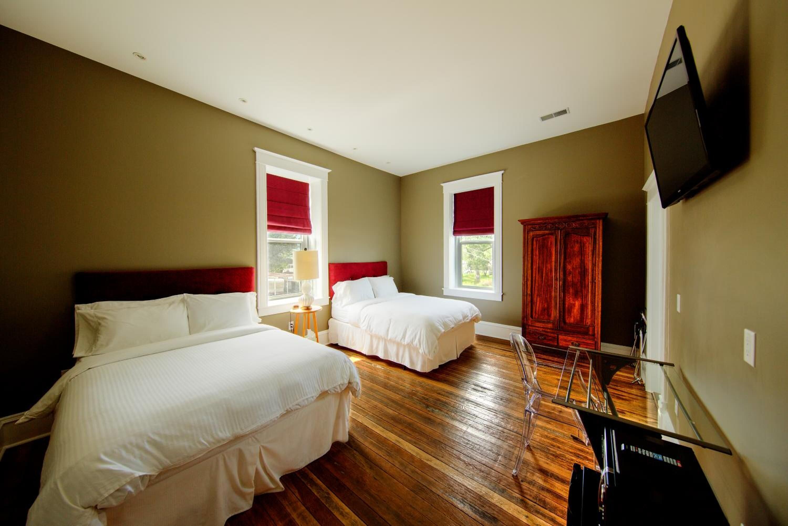A hotel room with two beds, wooden flooring, a TV, and a wardrobe.