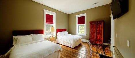 A hotel room with two beds, wooden flooring, a TV, and a wardrobe.