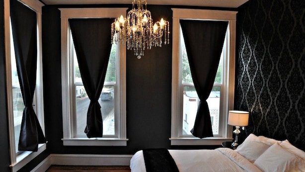 A bedroom with a large bed, a chandelier, and two windows with curtains. - The Harkness Hotel (McCammon)