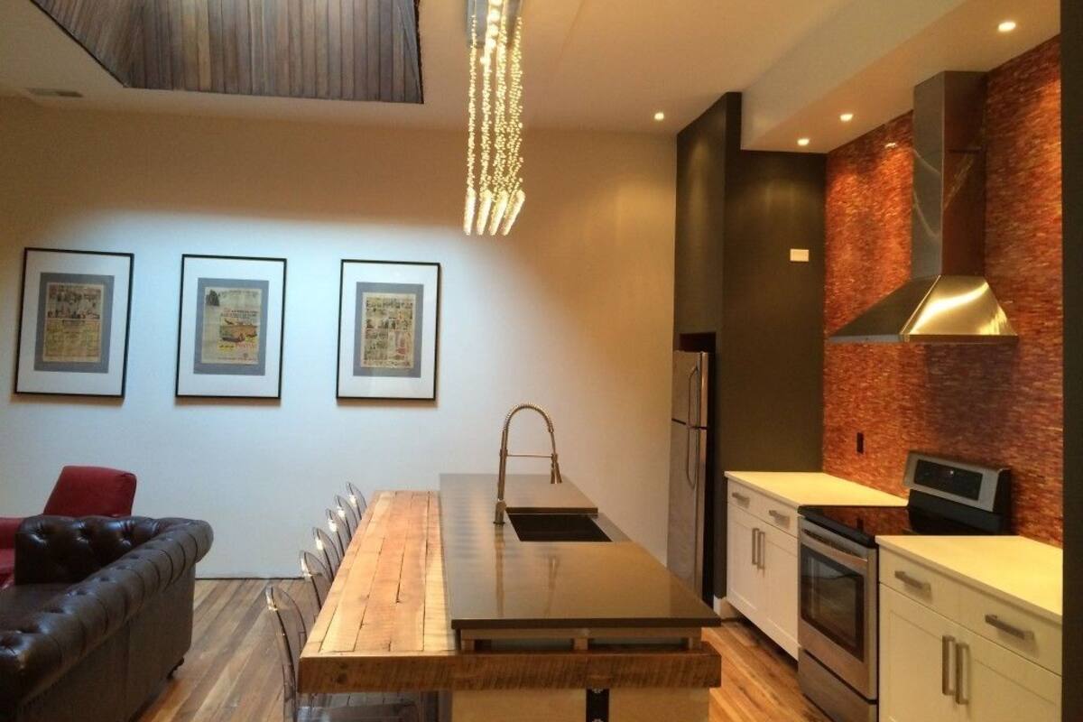 A modern kitchen with a wooden island, stainless steel appliances, and a red brick backsplash.