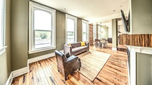 A spacious living room with large windows, a gray sofa, a leather armchair, and a wooden floor. - The Harkness Hotel (McCammon)