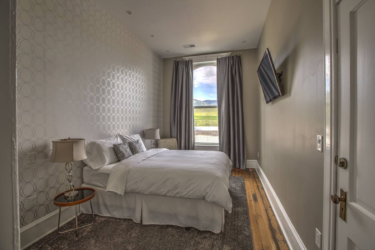 A bedroom with a bed, a nightstand, a lamp, and a TV mounted on the wall.
