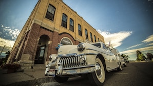 A vintage car parked in front of a brick building with a sign that reads "Harkness". - The Harkness Hotel (McCammon)