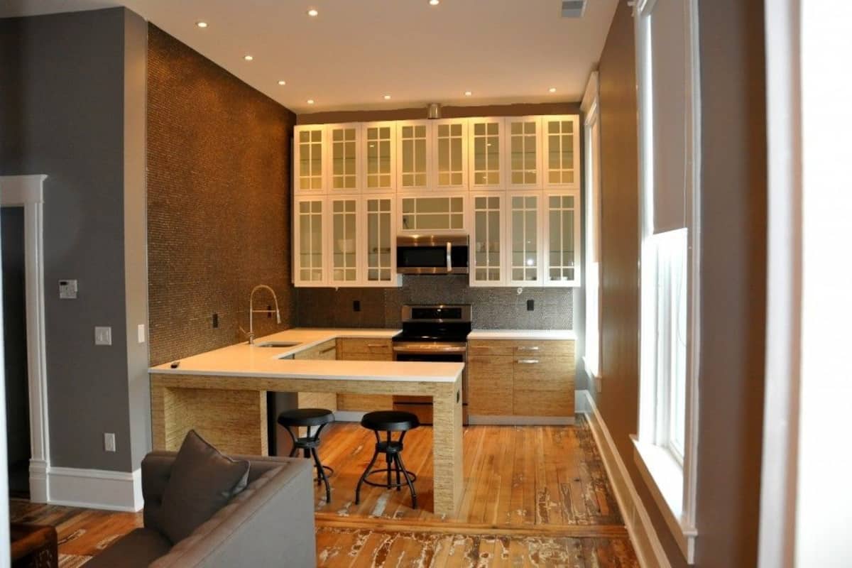 A modern kitchen with a central island, bar stools, and a microwave.