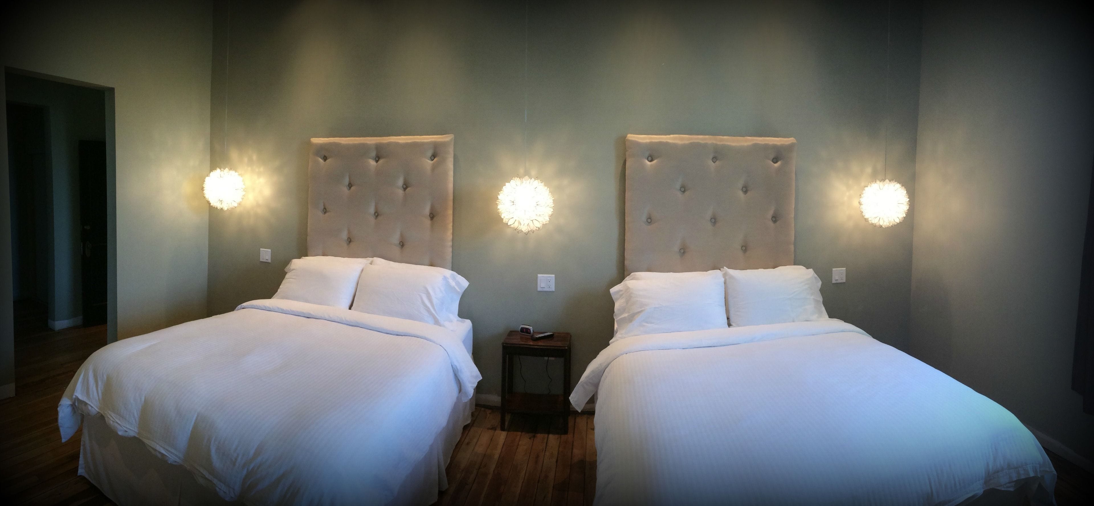 Twee bedden met gestoffeerde hoofdborden, wit beddengoed en wandlampen.