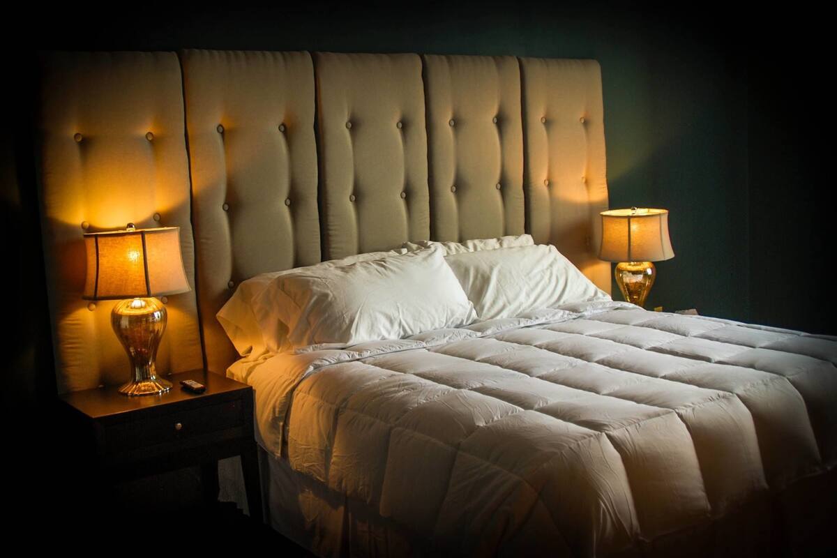 A neatly made bed with a tufted headboard, two bedside lamps, and a dark wall.