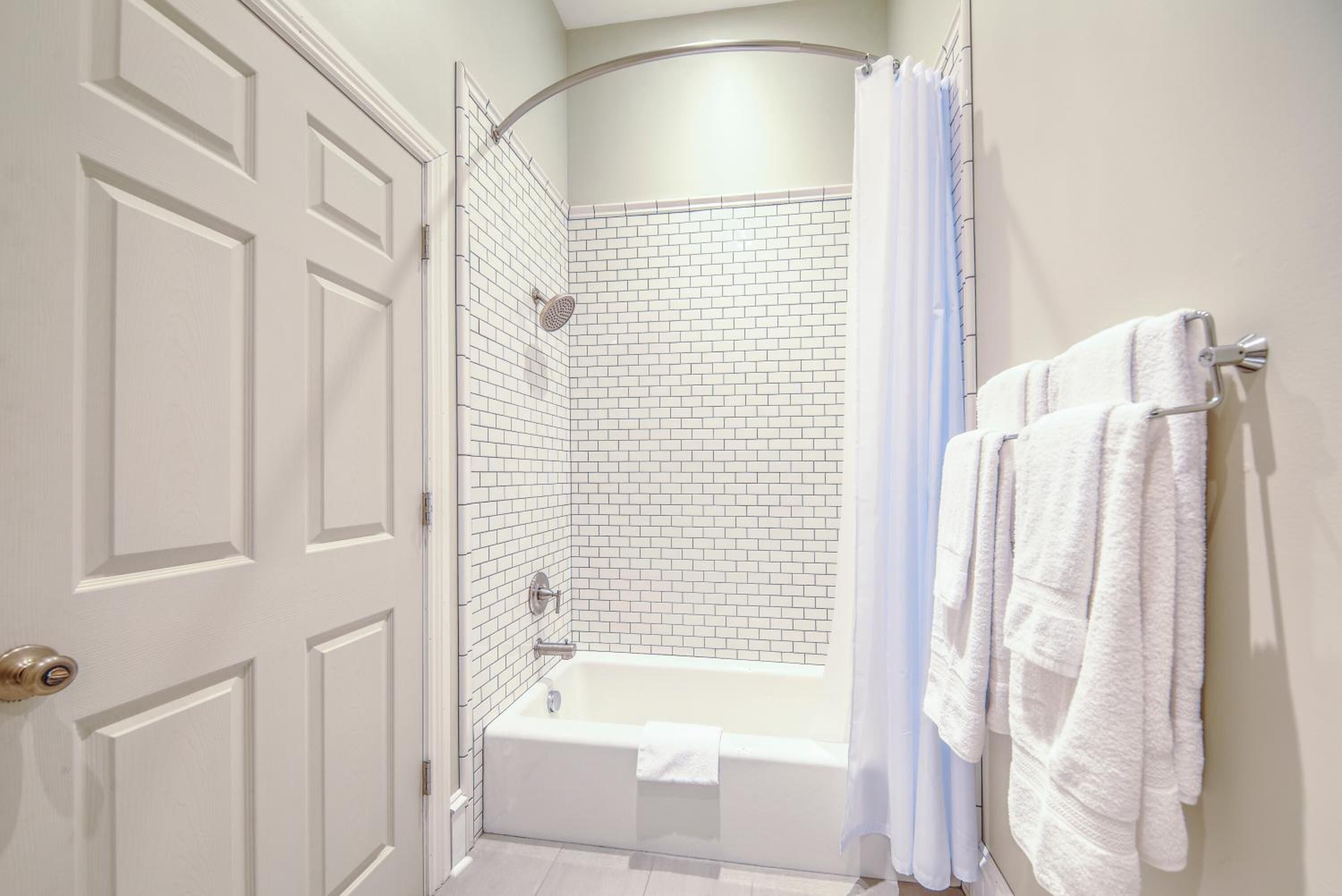 Ein Badezimmer mit einer weißen Badewanne, einer Dusche mit weißem Duschvorhang und einem Handtuchhalter mit weißen Handtüchern.