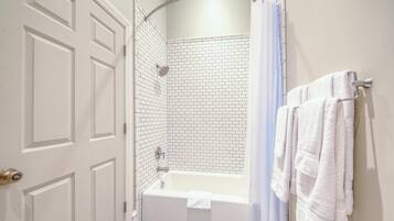 Ein Badezimmer mit einer weißen Badewanne, einer Dusche mit weißem Duschvorhang und einem Handtuchhalter mit weißen Handtüchern.