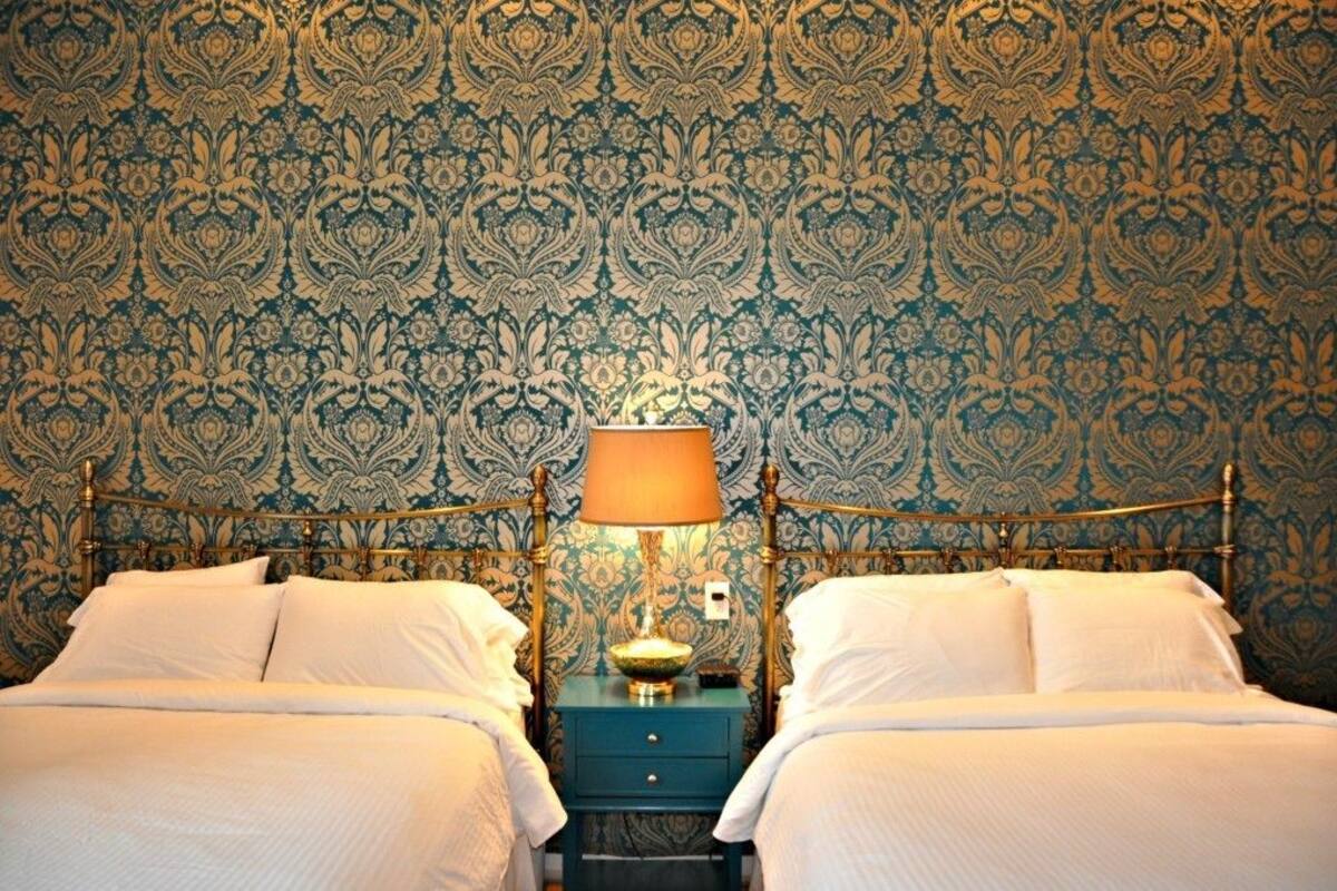 A double bed with a blue nightstand and a lamp, set against a patterned wallpaper.