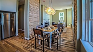 A modern kitchen with stainless steel appliances, a dining area with a wooden table and chairs, and a large chandelier. - The Harkness Hotel (McCammon)