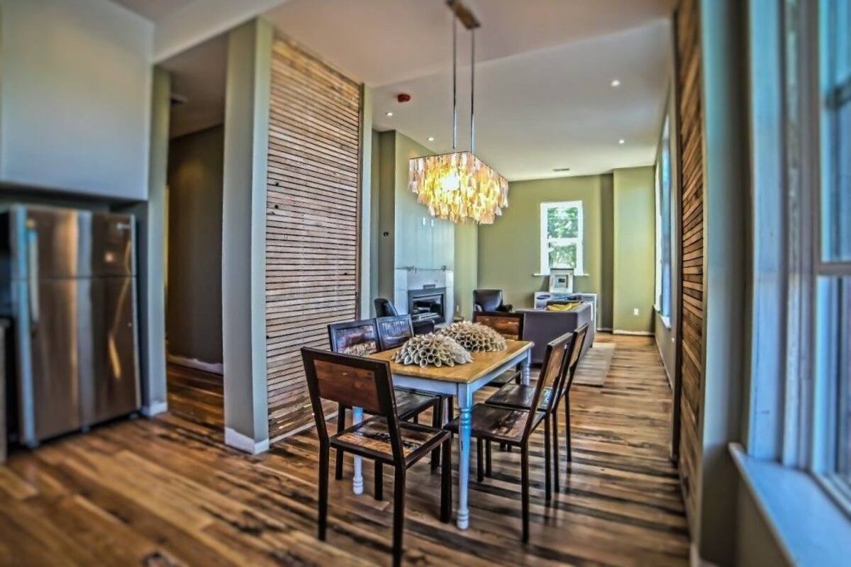 A modern kitchen with stainless steel appliances, a dining area with a wooden table and chairs, and a large chandelier.