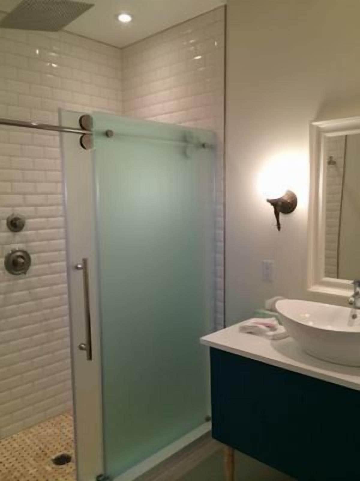 A modern bathroom with a glass shower enclosure, a white sink, and a mirror with a light.