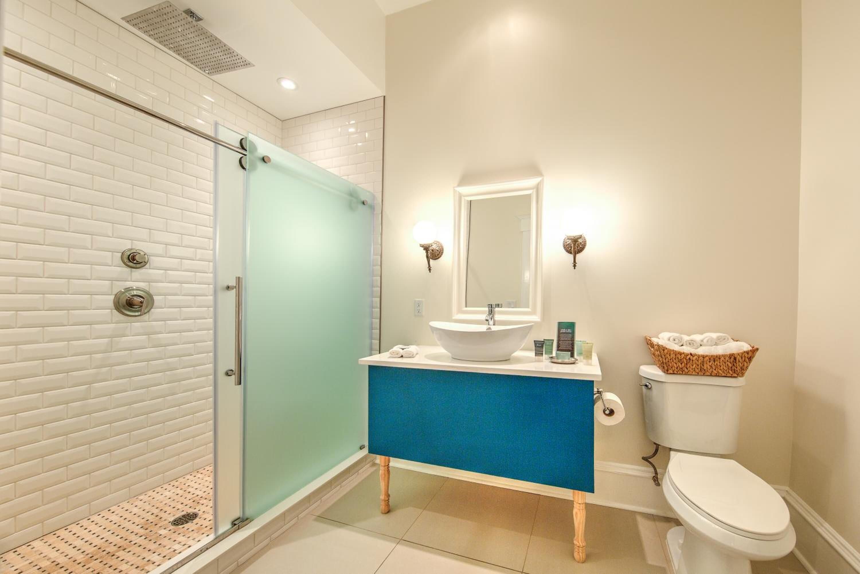 A modern bathroom with a glass shower enclosure, a white toilet, a blue vanity, and a white sink.