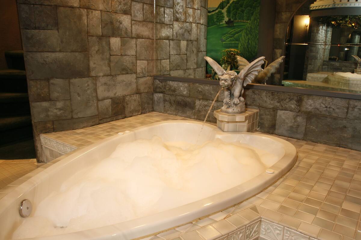 A large, oval-shaped bathtub with a stone wall backdrop and a decorative sculpture.