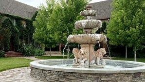 A multi-tiered stone fountain with lion statues, surrounded by a stone wall and lush greenery. - Black Swan Inn (Pocatello)