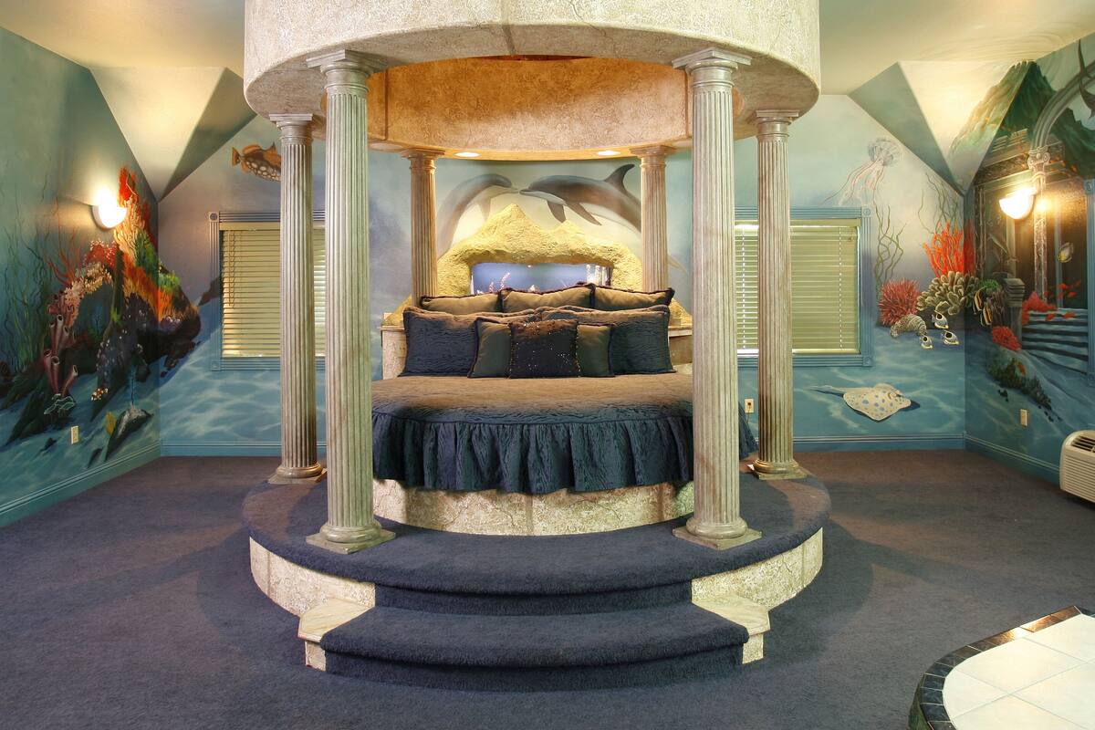 A circular bed with a canopy, a staircase leading to it, and a mural of underwater scenery on the walls.