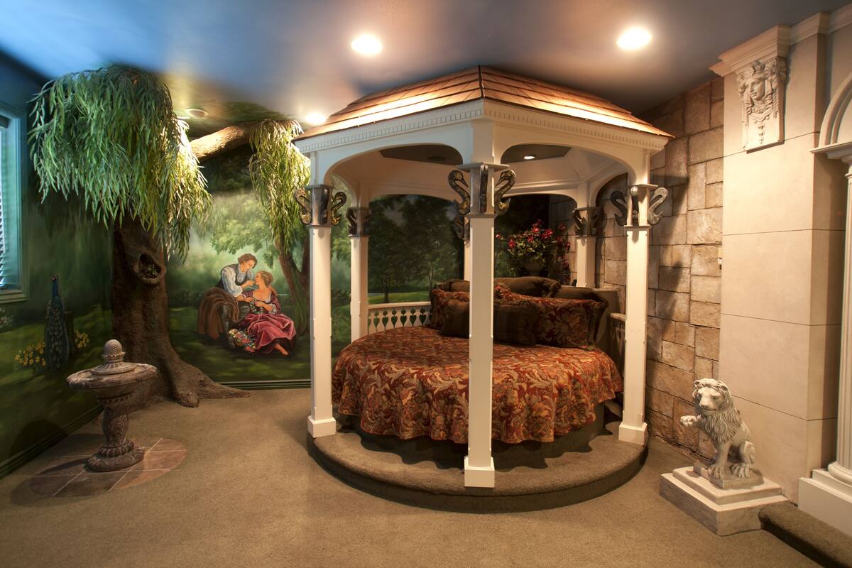 A bedroom with a canopy bed, a mural of a couple, and a statue of a lion.
