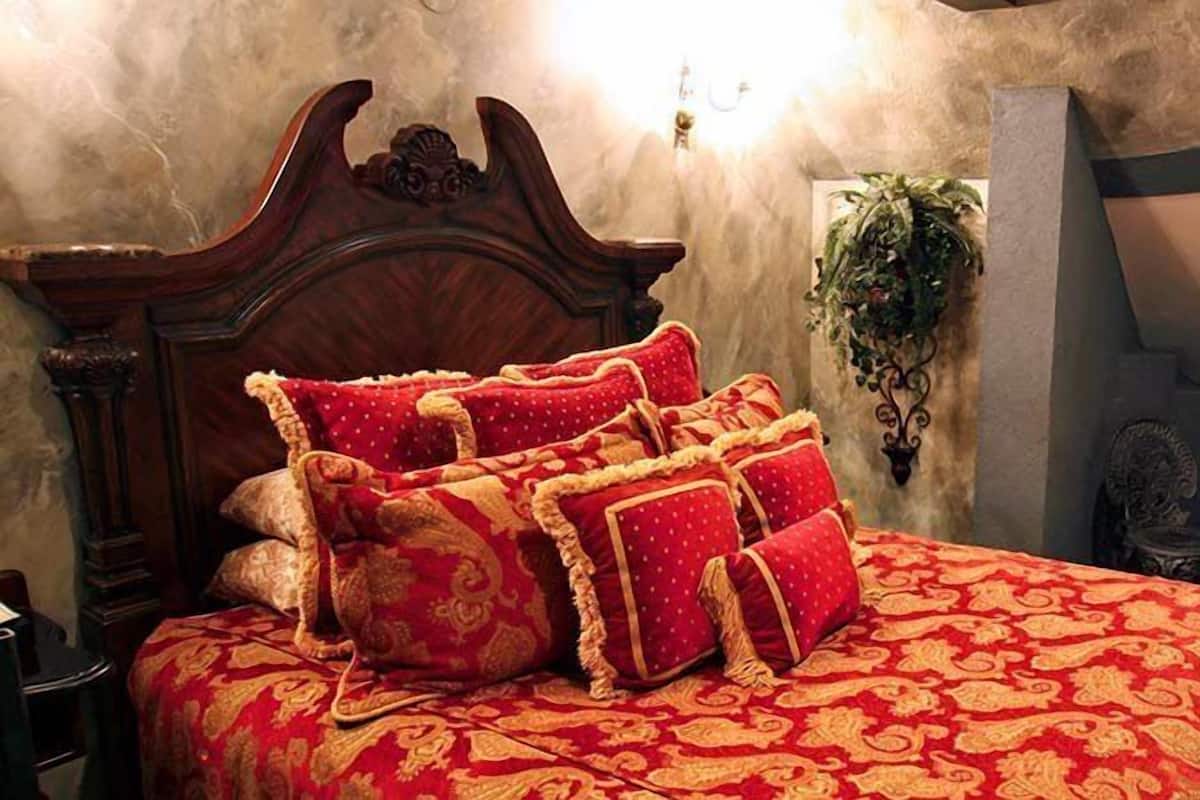 A bedroom with a large bed, ornate headboard, and a red patterned bedspread.