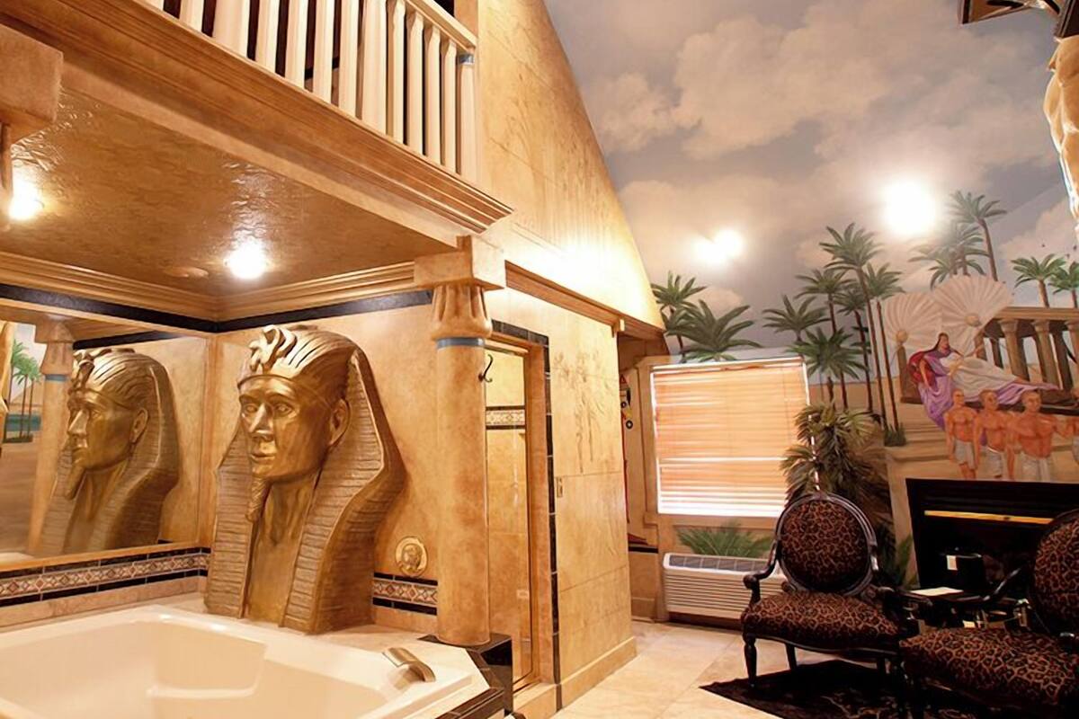 A luxurious bathroom with a large bathtub, Egyptian-themed decor, and a balcony with a view of palm trees.